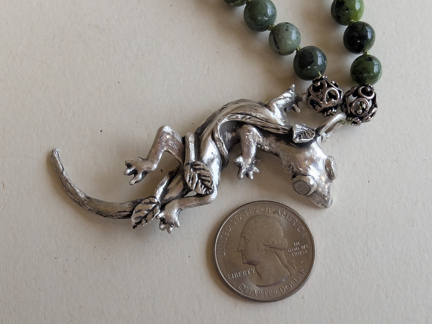 Silver lizard pendant on a necklace with beads, next to a quarter for scale.