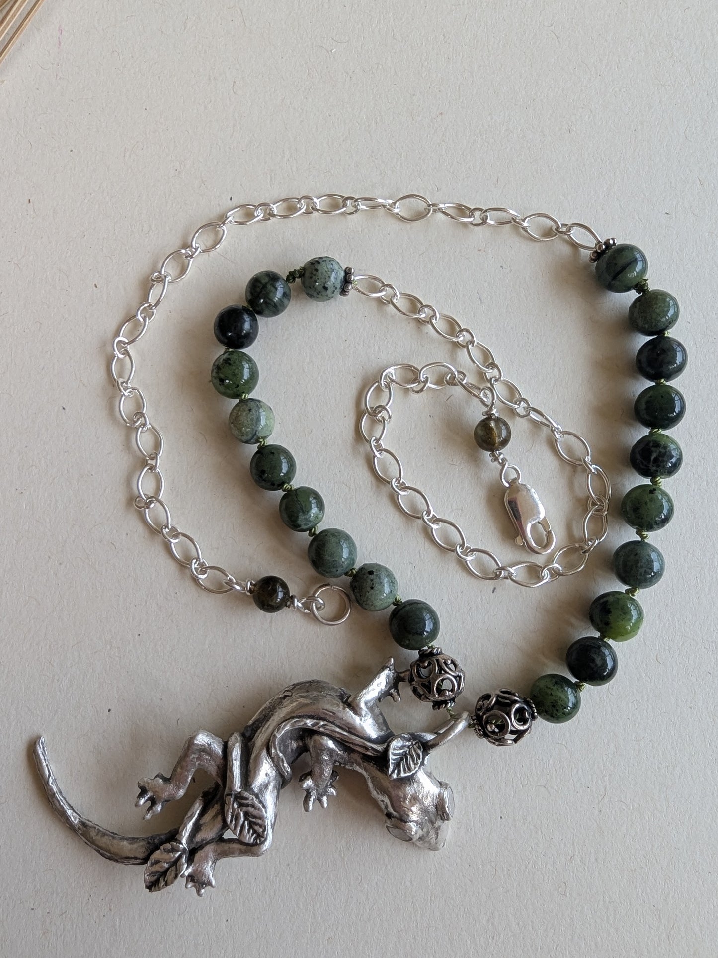 Necklace with green beads and silver lizard pendant on a light background
