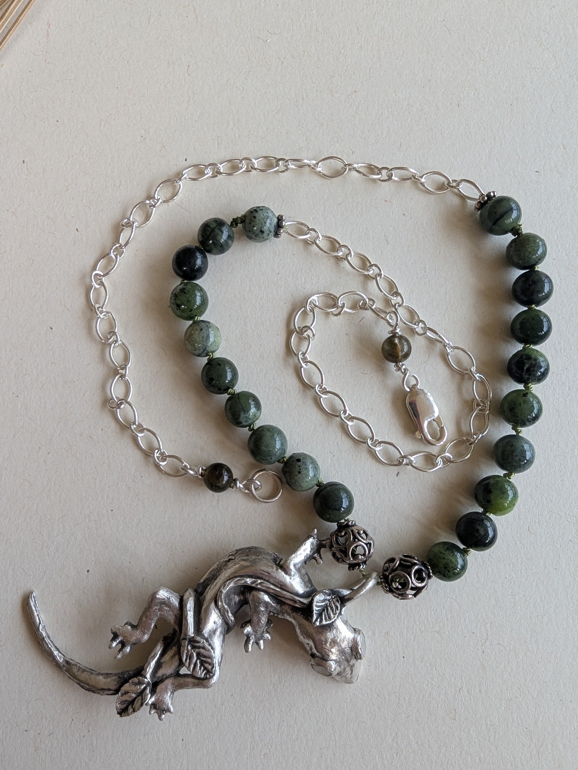 Necklace with green beads and silver lizard pendant on a light background