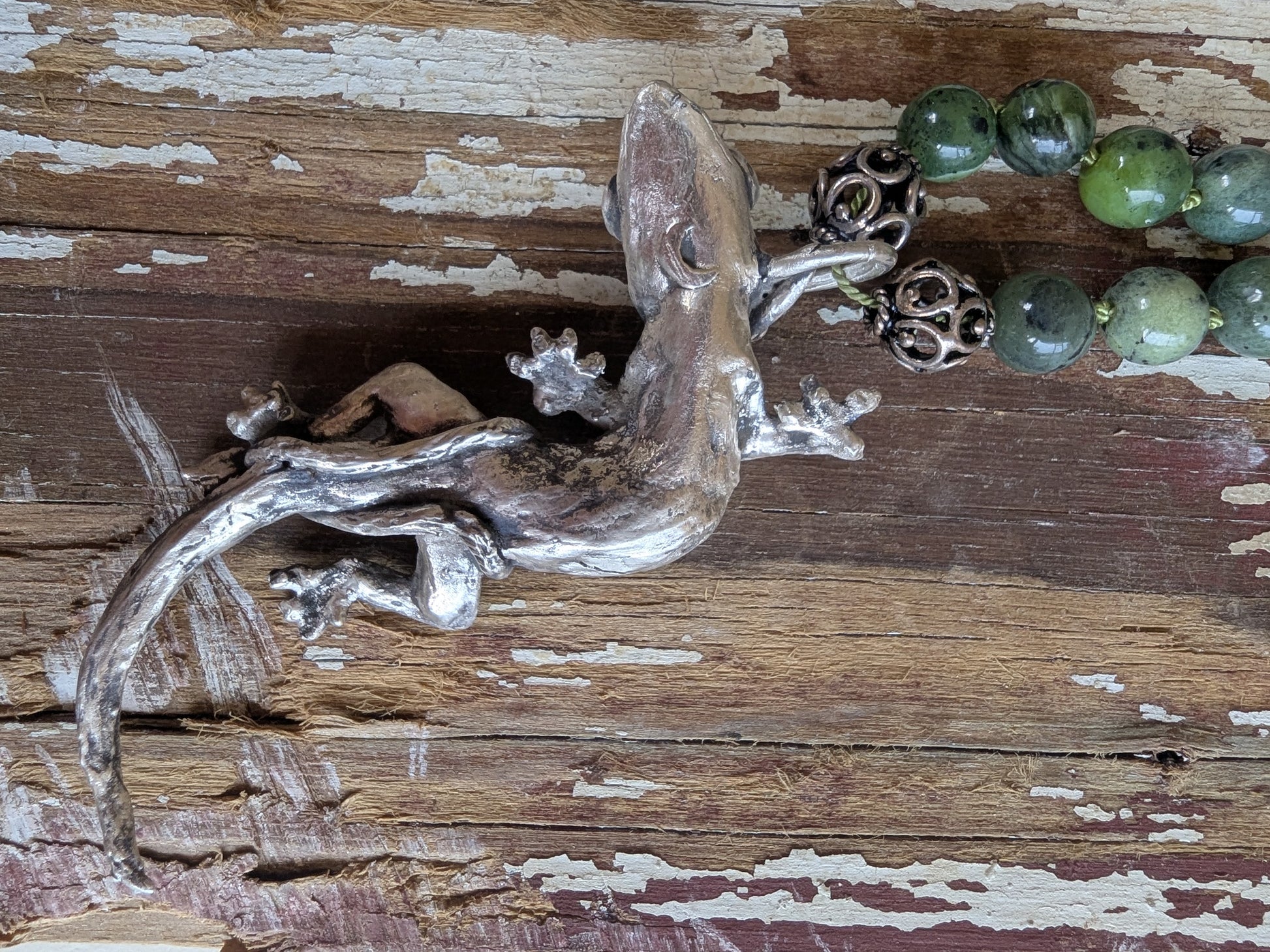Underside of silver lizard pendant and green beaded necklace on a wooden surface