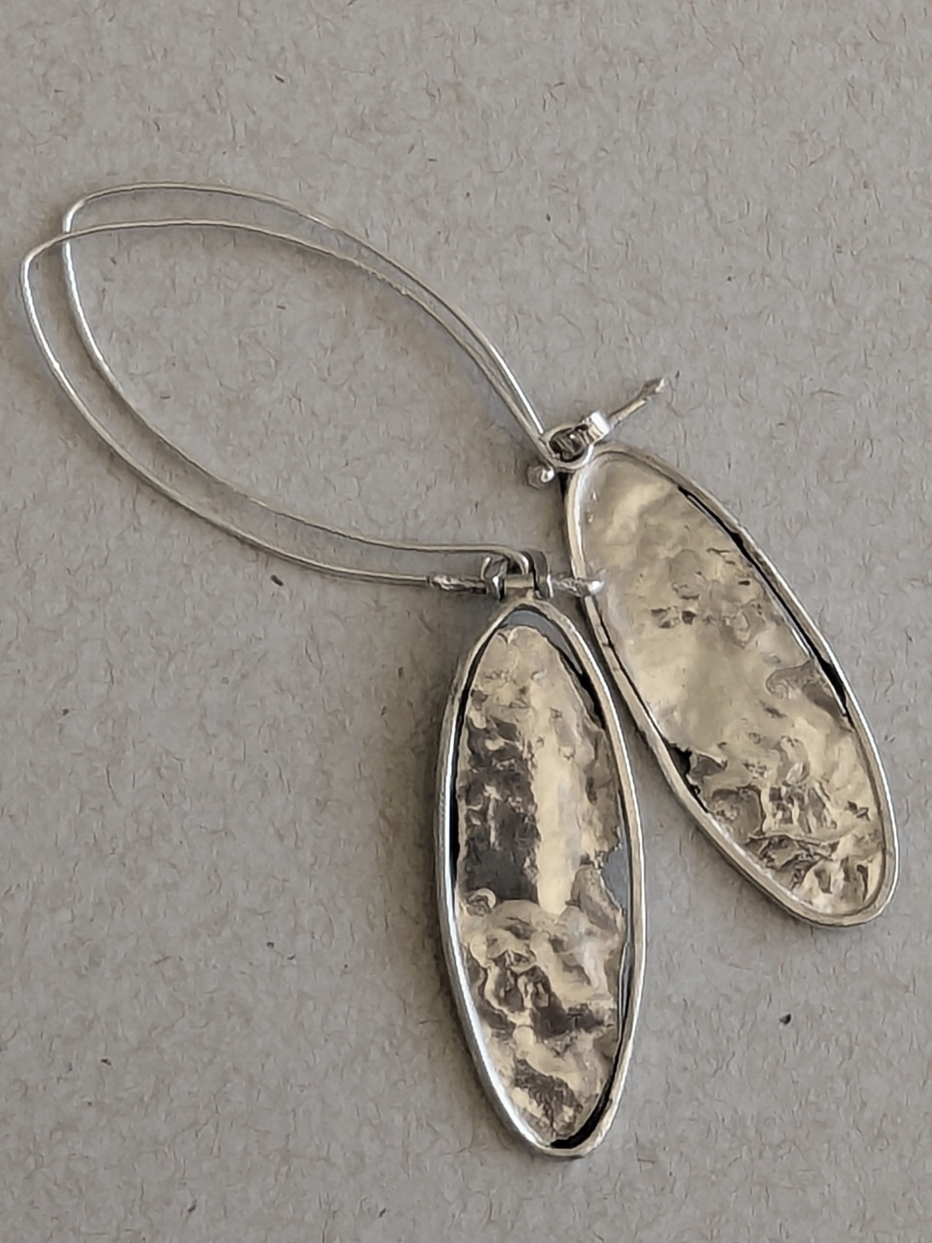 Reverse side of oval silver earrings with textured design on a gray background