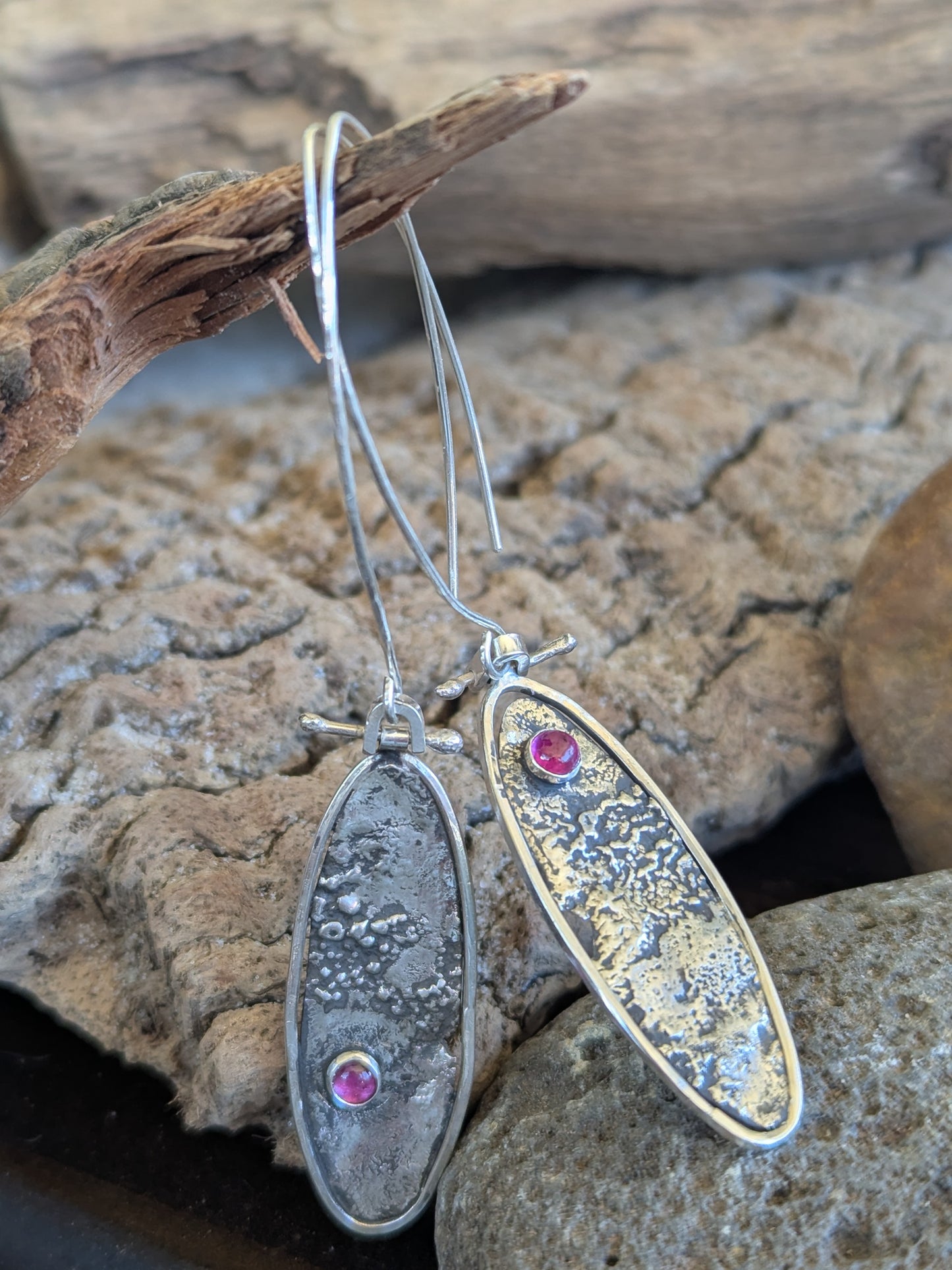 Silver oval earrings with ruby gemstones on a stone surface
